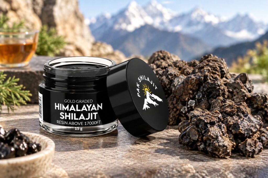 Pak Shilajit jar beside raw shilajit rocks and a cup of tea on a stone ledge, with snow-covered Himalayan peaks behind