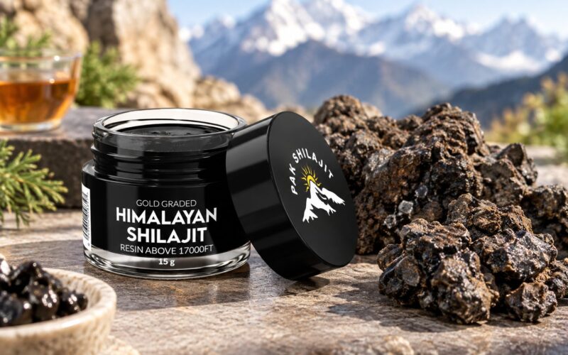 Pak Shilajit jar beside raw shilajit rocks and a cup of tea on a stone ledge, with snow-covered Himalayan peaks behind