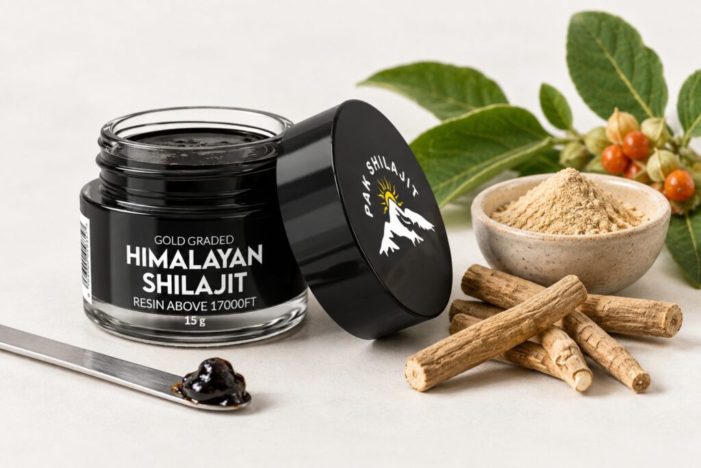 Pak Shilajit jar of gold-graded Himalayan shilajit resin beside dried ashwagandha root, a bowl of ashwagandha powder and the plant with its orange berries