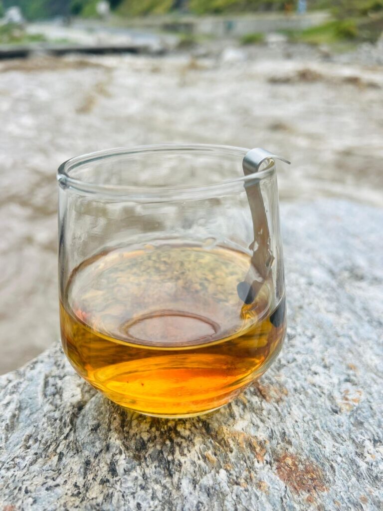 Fully dissolved shilajit in water, an even golden-amber with no sediment, on a rock beside a Himalayan river